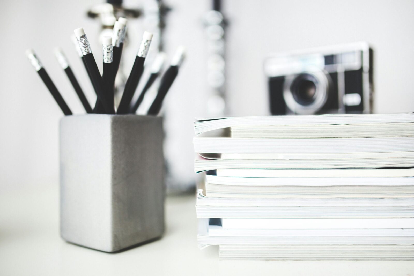 Organized workspace featuring pencils in holder and stacked magazines with a vintage camera in the background.